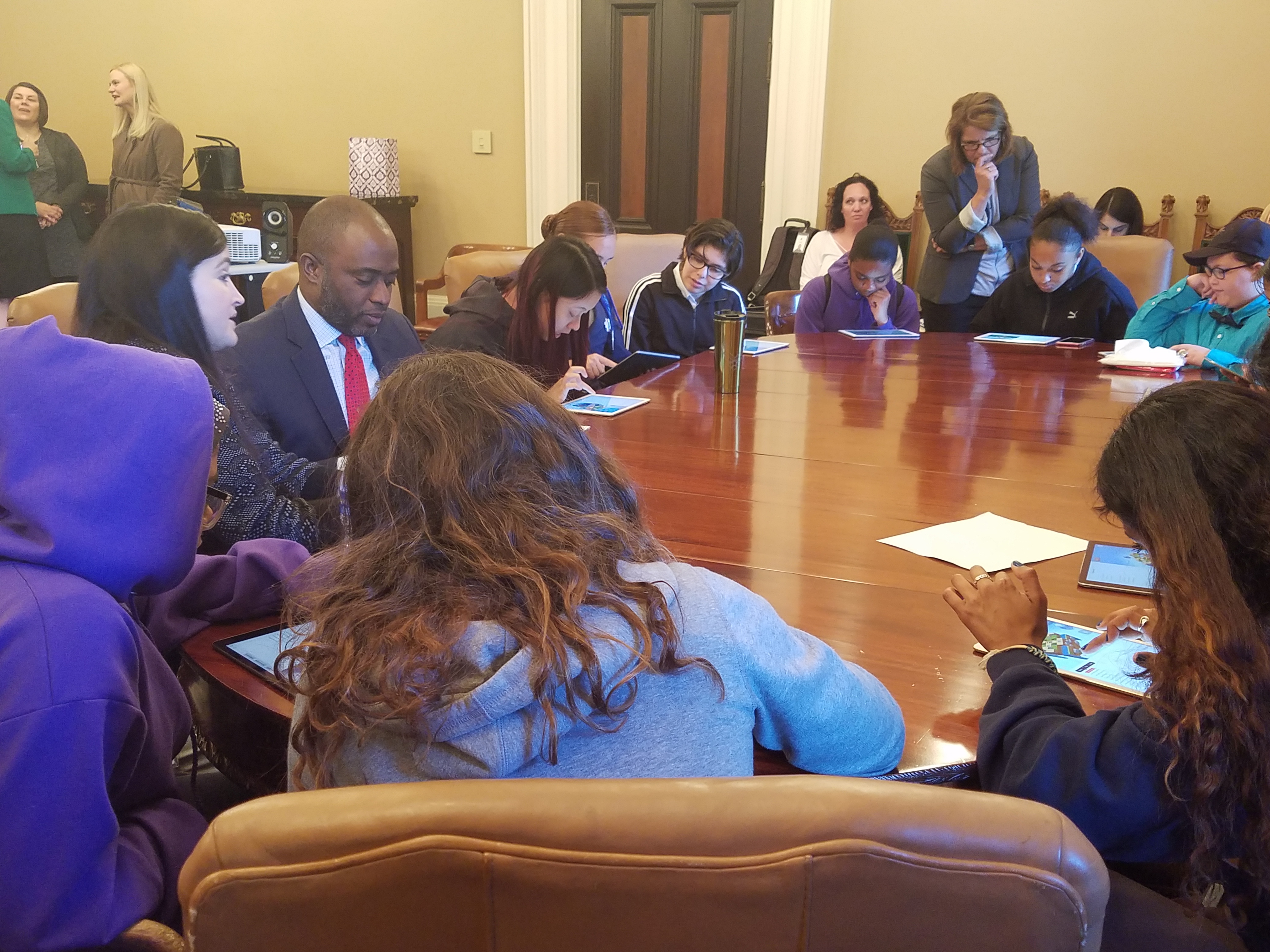 Students sitting with Tony Thurmond around a table for a coding demonstration
